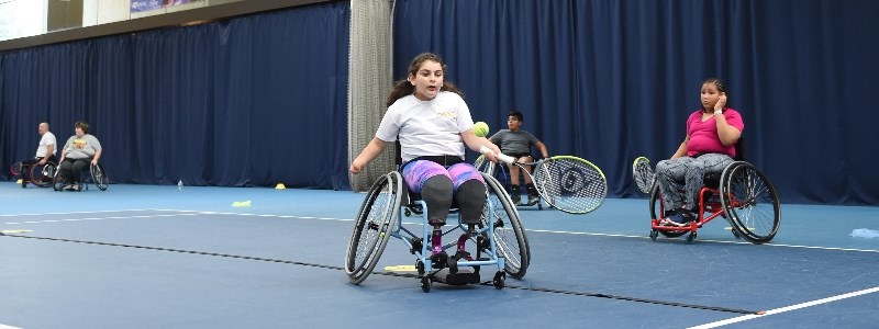 A girl in a wheelchair hitting a tennis ball
