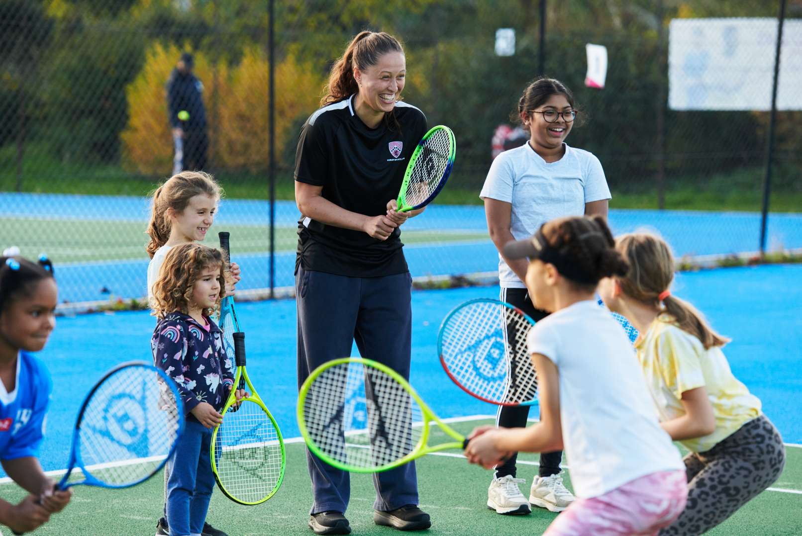 Female coach surrounded by children holding tennis rackets
