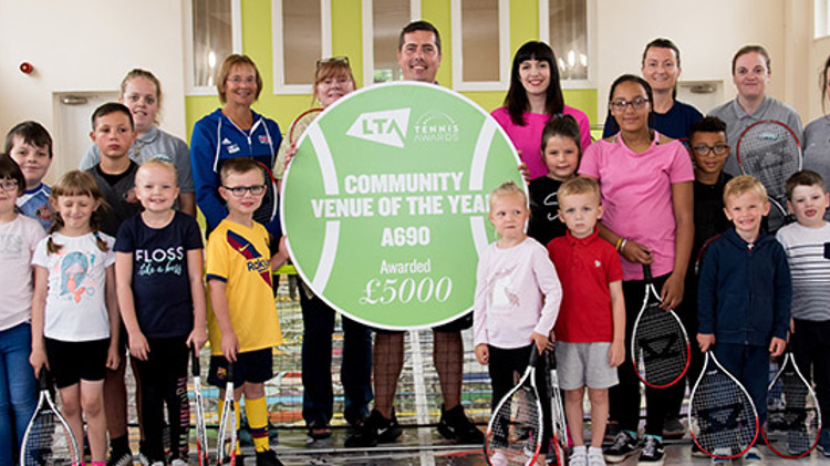 Adults and children holding tennis rackets and a community of the year award