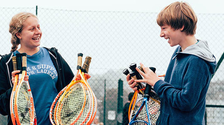 two children smiling holding tennis rackets