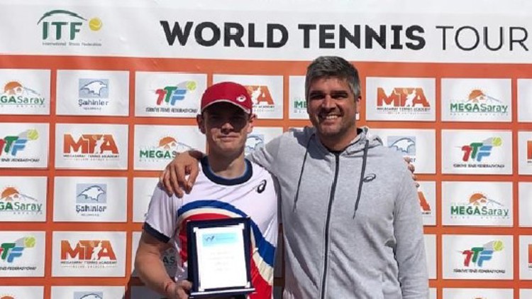 jack pinnington jones standing  besides adult holding trophy with  itf world tennis tour board at the back