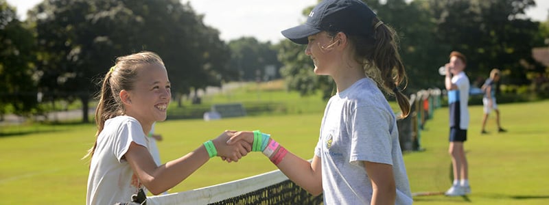 two young female tennis players shaking hands over the net