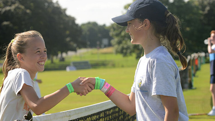 two young female tennis players shaking hands over the net