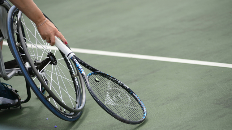 Close-up image of wheelchair on court with a tennis racket