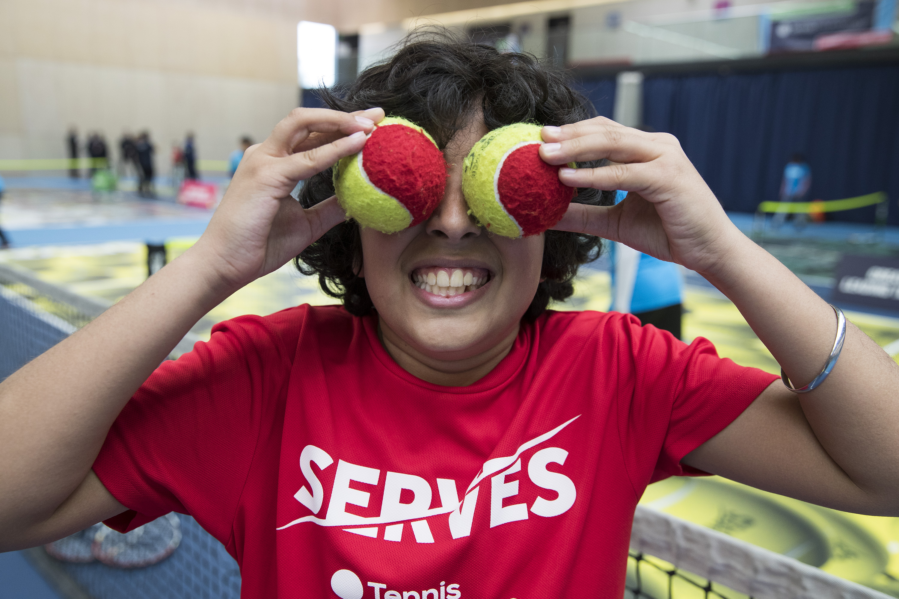 Boy holding tennis balls over his face smiling