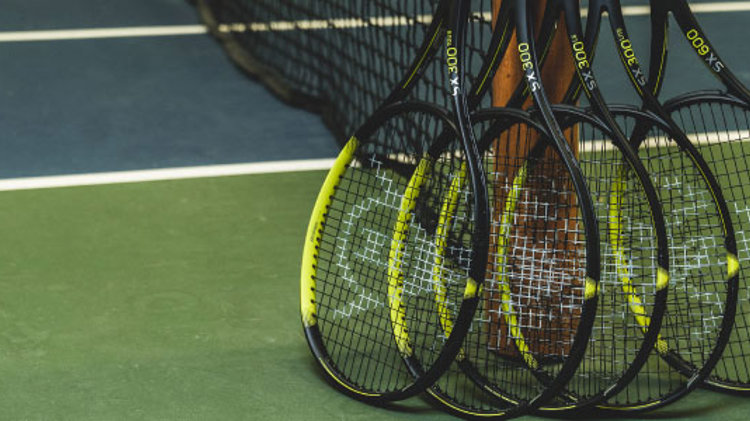 image of 5 black and yellow tennis dunlop  rackets leaning against a tennis net