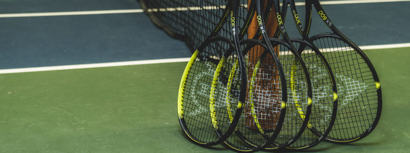 image of 5 black and yellow tennis dunlop  rackets leaning against a tennis net