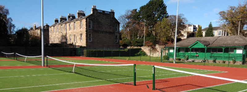 4 artificial grass courts with a wooden pavilion at the back  of the courts and houses to left