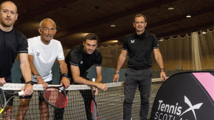 four tennis players standing and leaning on the net with rackets in hand next to a tennis scotland  banner