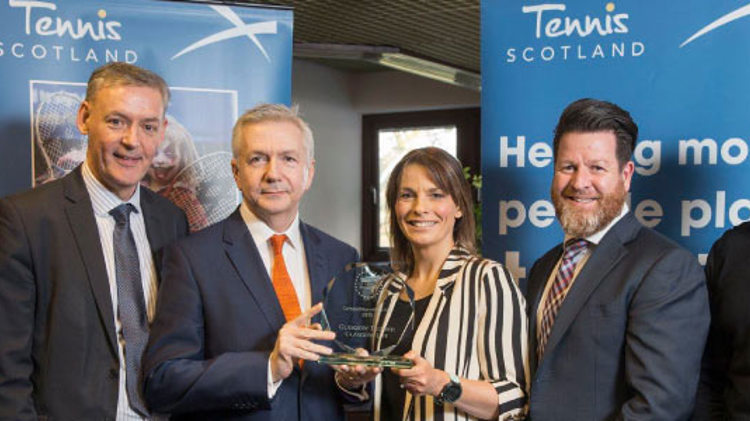 a group of winners lined up with two holding a glass tennis scotland trophy