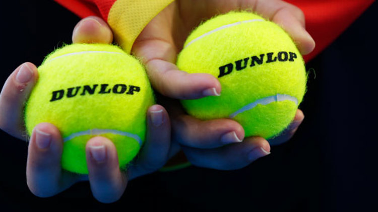 close up image of two dunlop tennis balls held in hands that are crossed