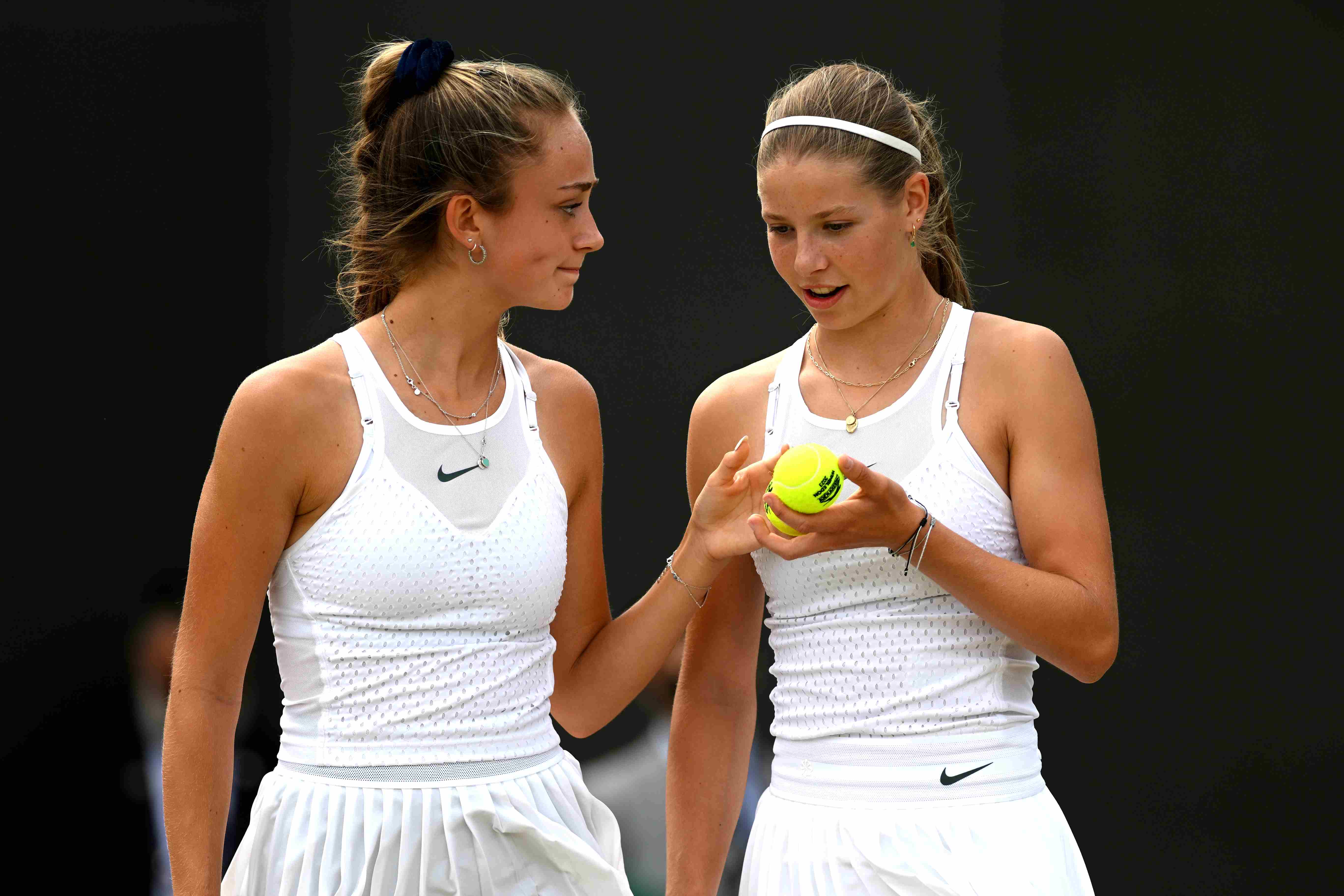 Isabelle Lacy smiling at Hannah Klugman who is holding a tennis ball on court at the Wimbledon Girls doubles final