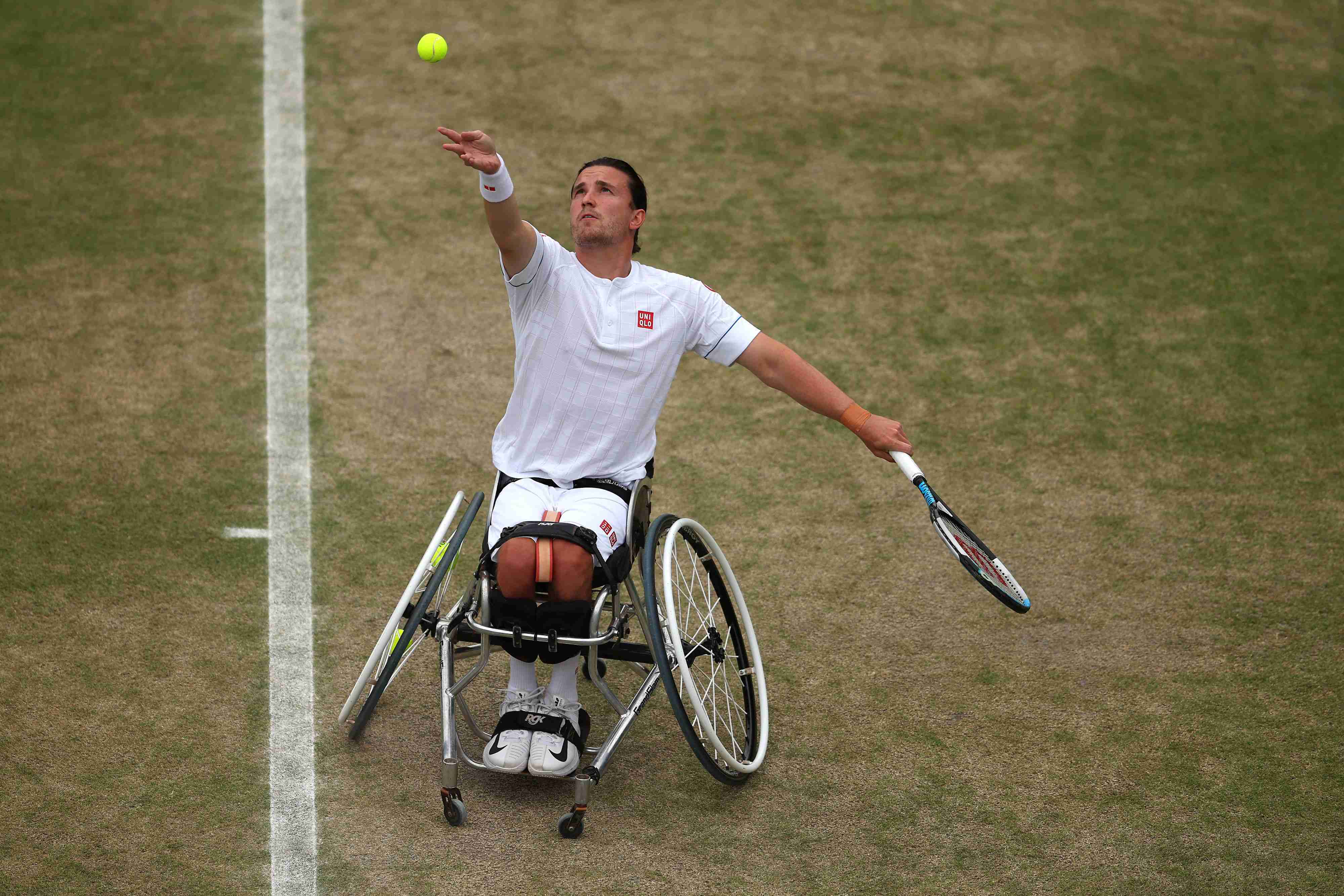 Wheelchair tennis player Gordon Reid throws tennis ball in the air and prepares to hit a serve on a grass court