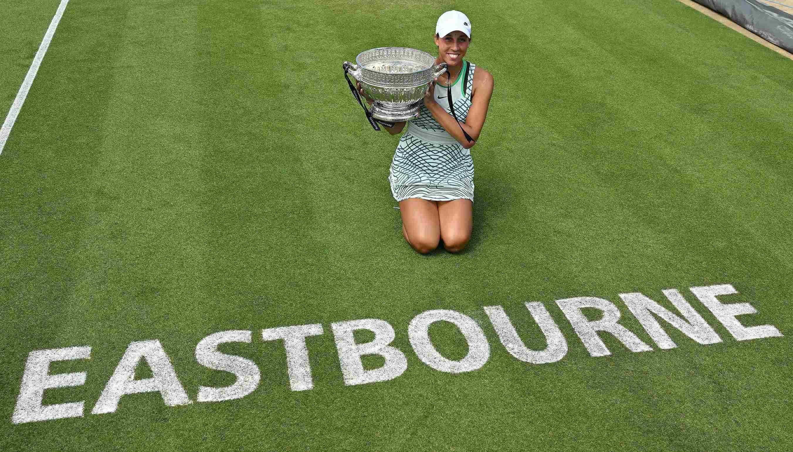 Madison Keys holding the Rothesay International trophy while kneeling down next to the Eastbourne logo on court