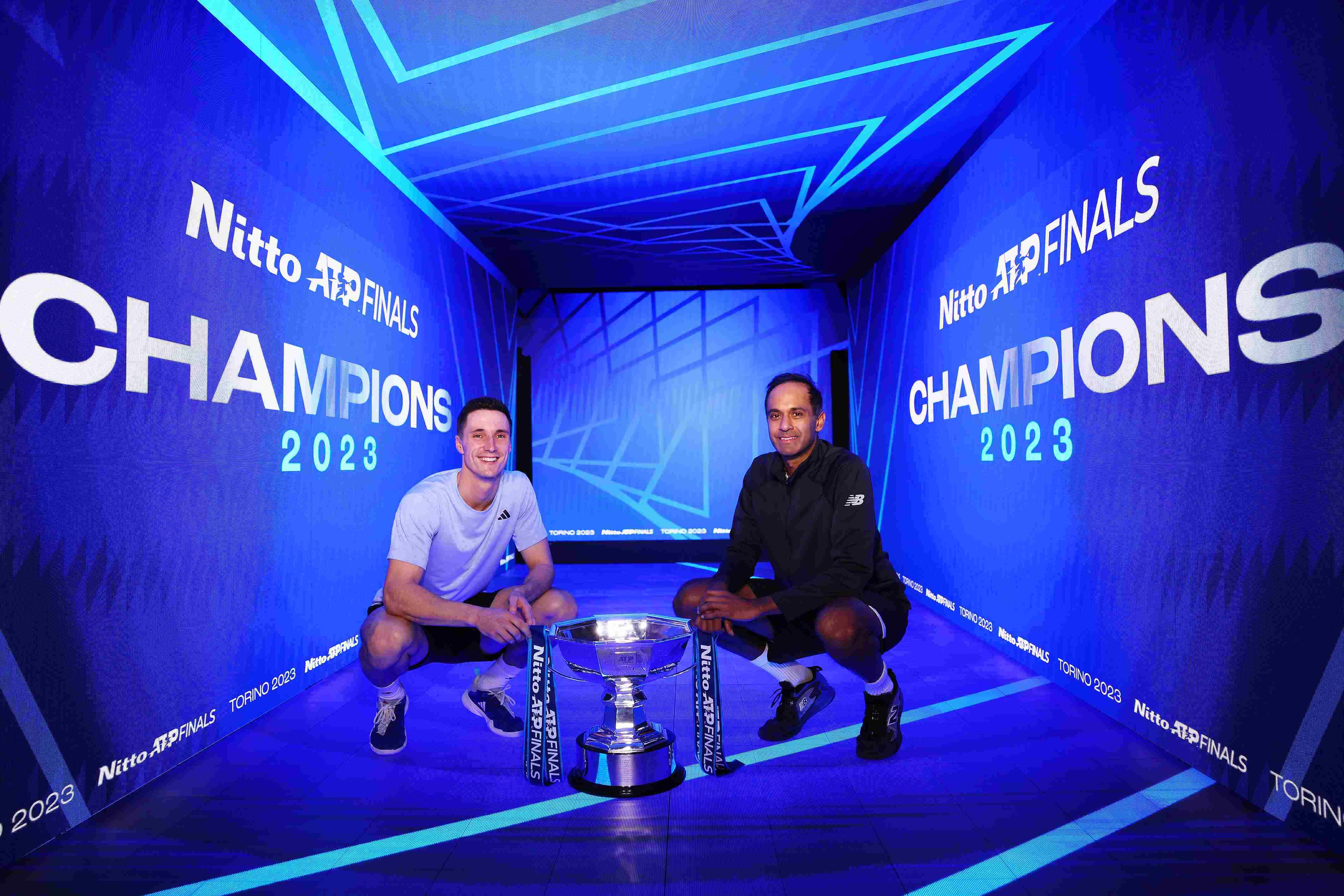Joe Salisbury and Rajeev Ram crouching down next to the Nitto ATP Finals trophy with a digital screen saying Champions behind them