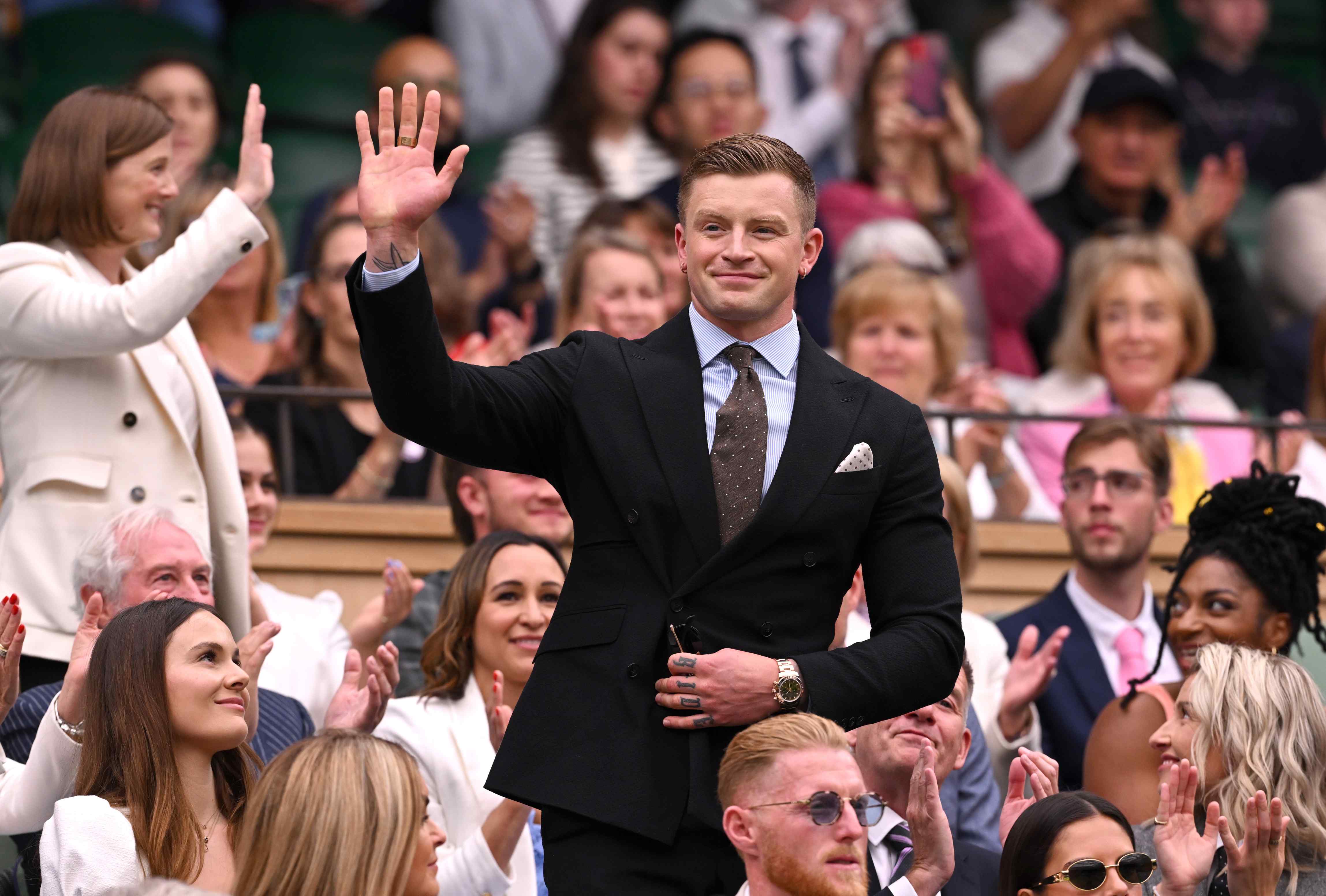 Adam Peatty, wearing a suit, while waving at the crowd at Wimbledon