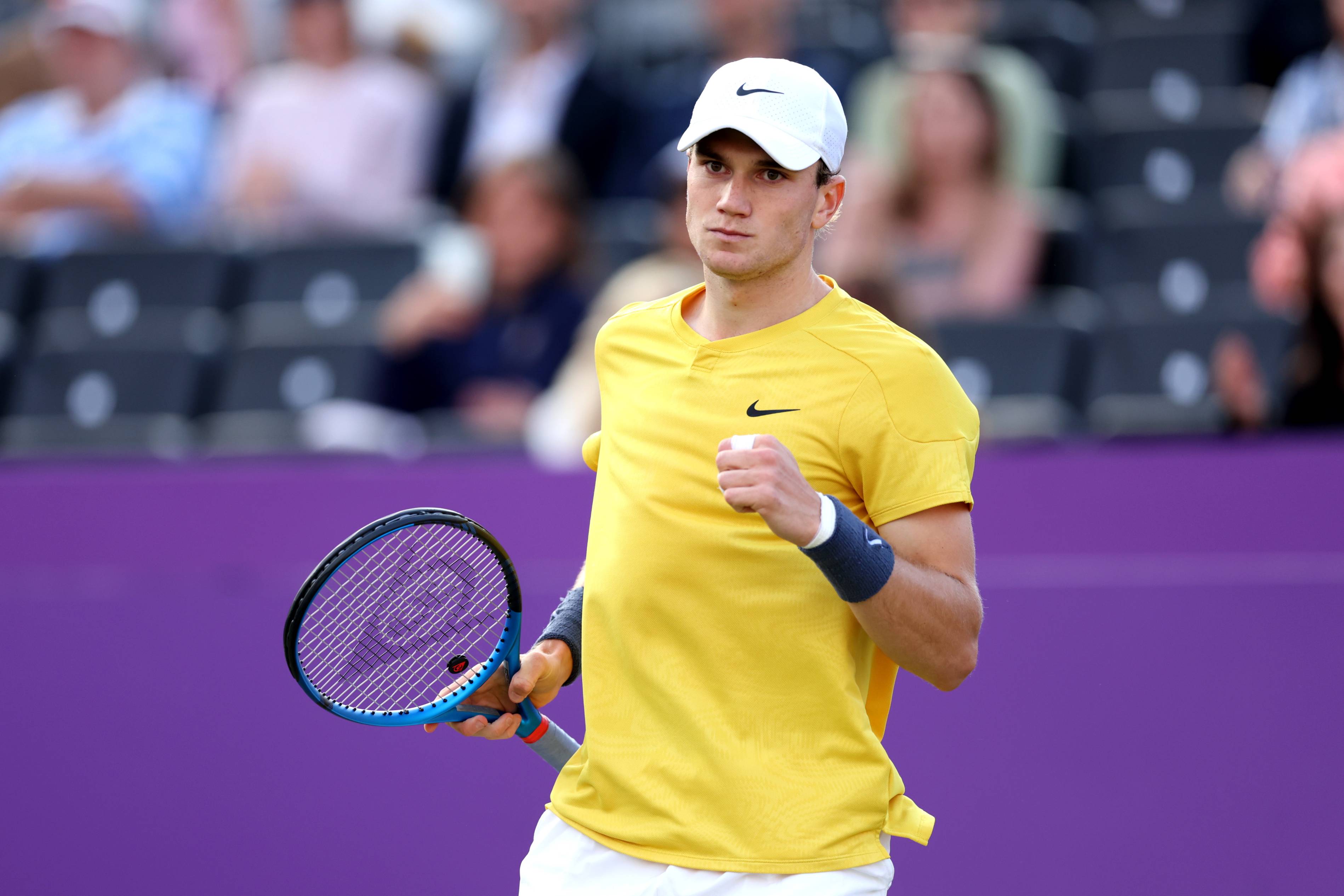 Jack draper wearing a yellow shirt and white hat clenching his fist on court at the cinch Championships while holding his tennis racket