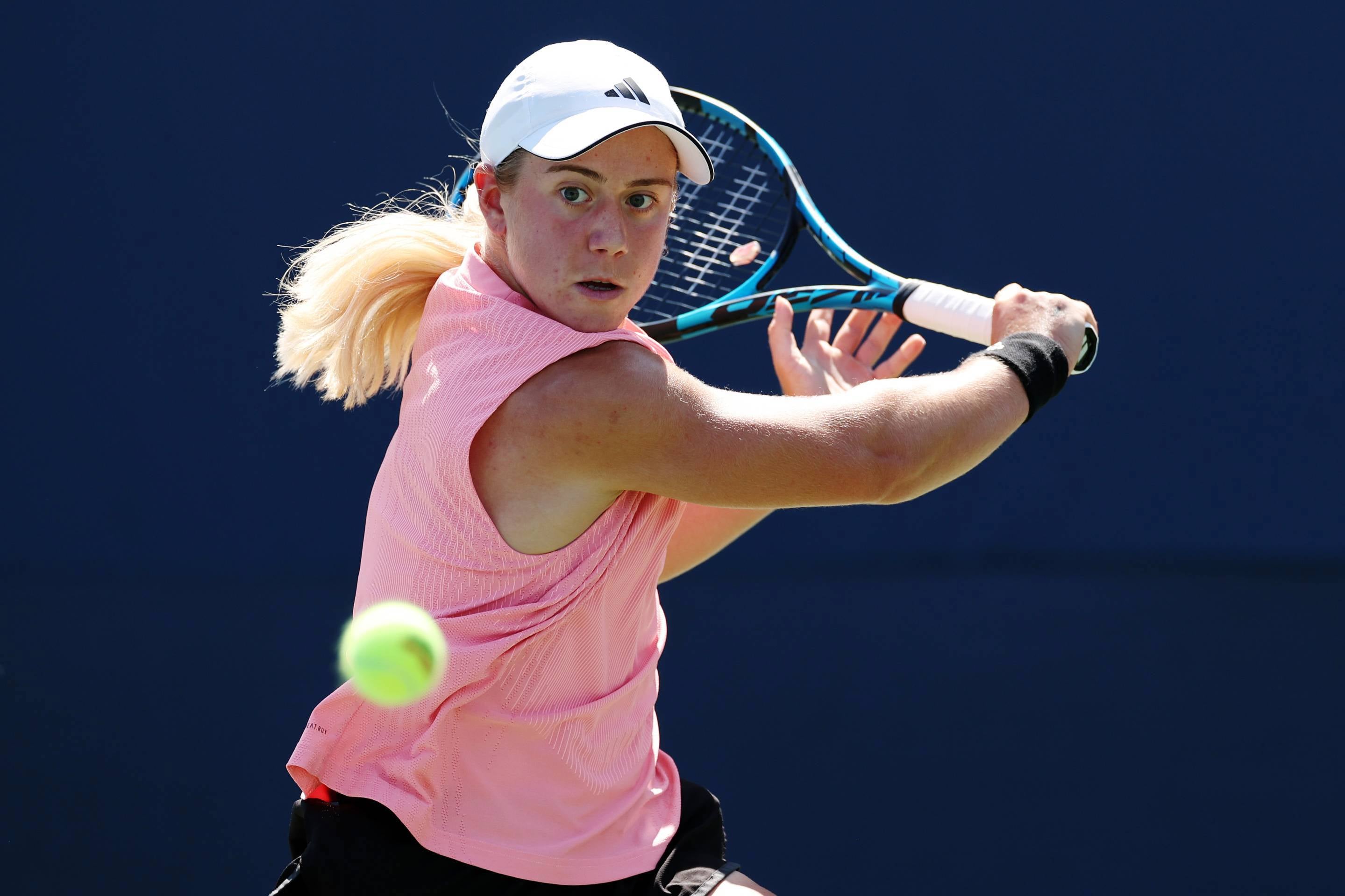 British tennis player Sonay Kartal wearing a pink top with a white Adidas hat while hitting a backhand slice at the US Open