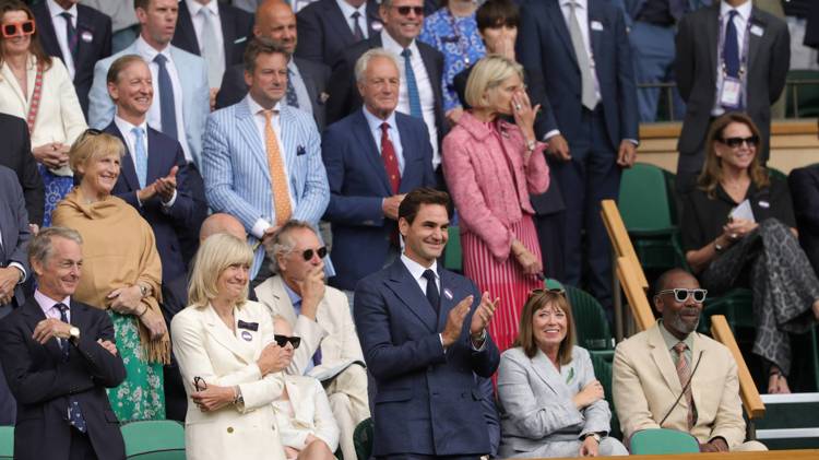The Royal Box guests with Roger Federer at the front at Wimbledon standing up smiling and clapping while looking onto court