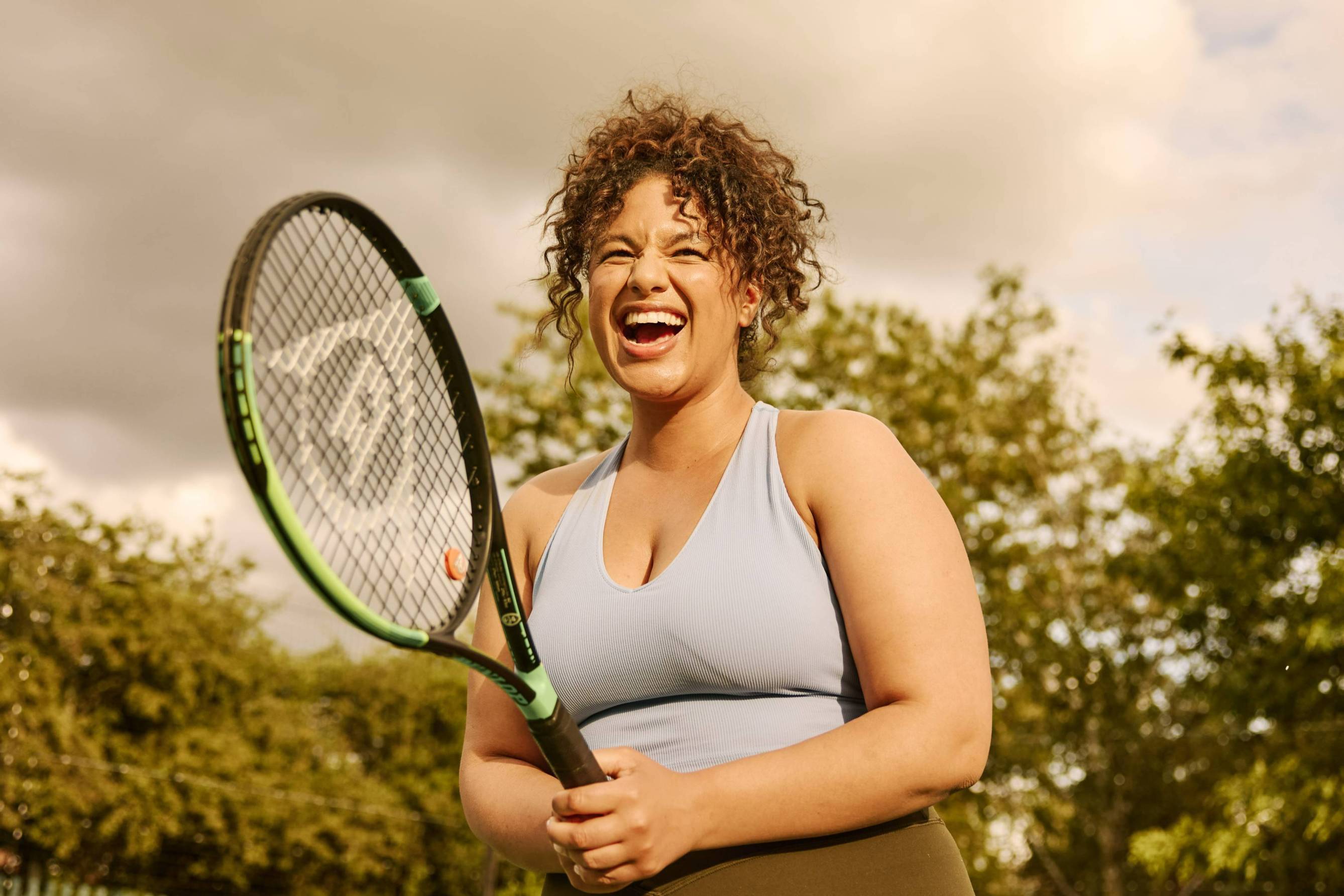 A woman laughing while holding a tennis racket on court