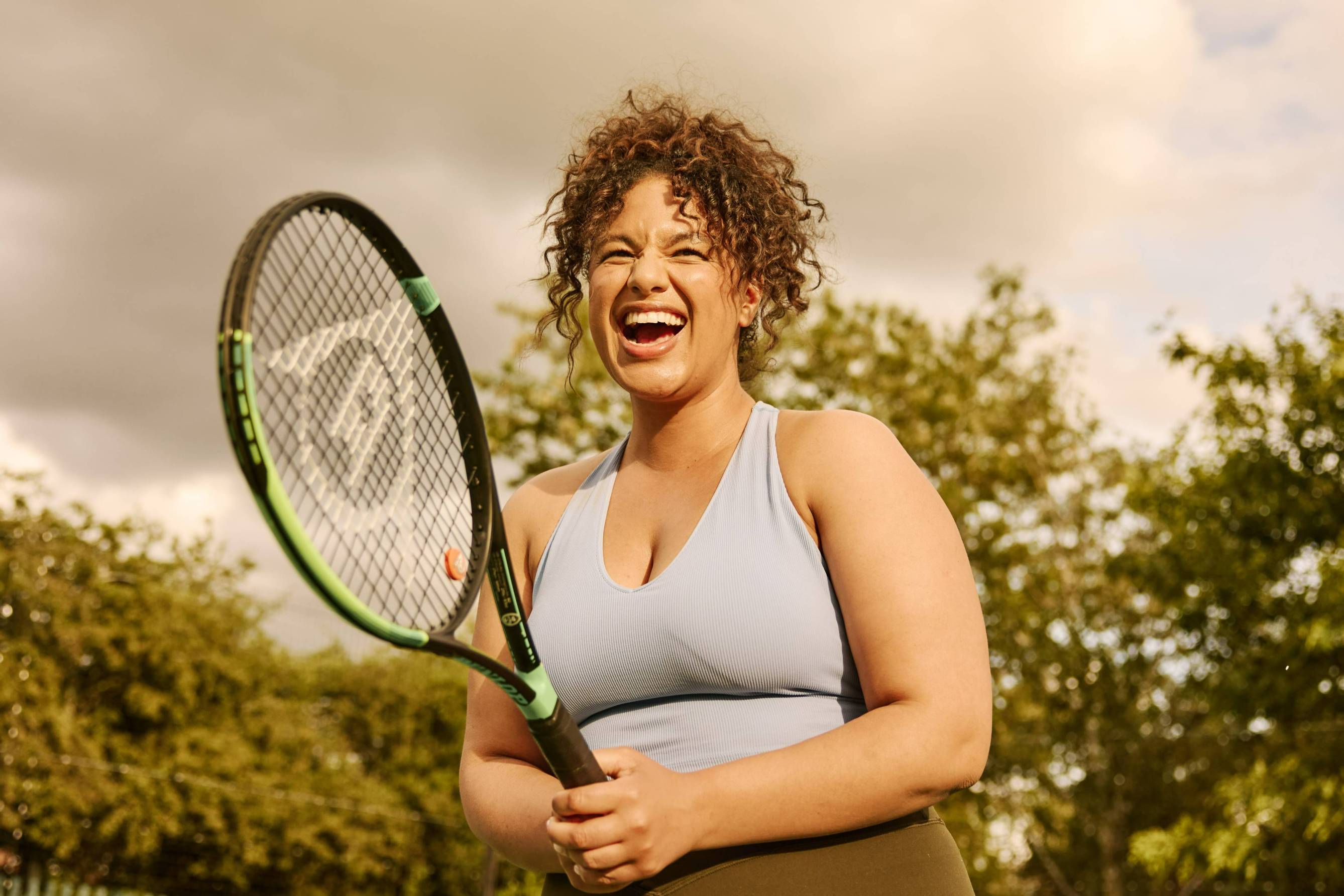 A woman laughing while holding a tennis racket on court