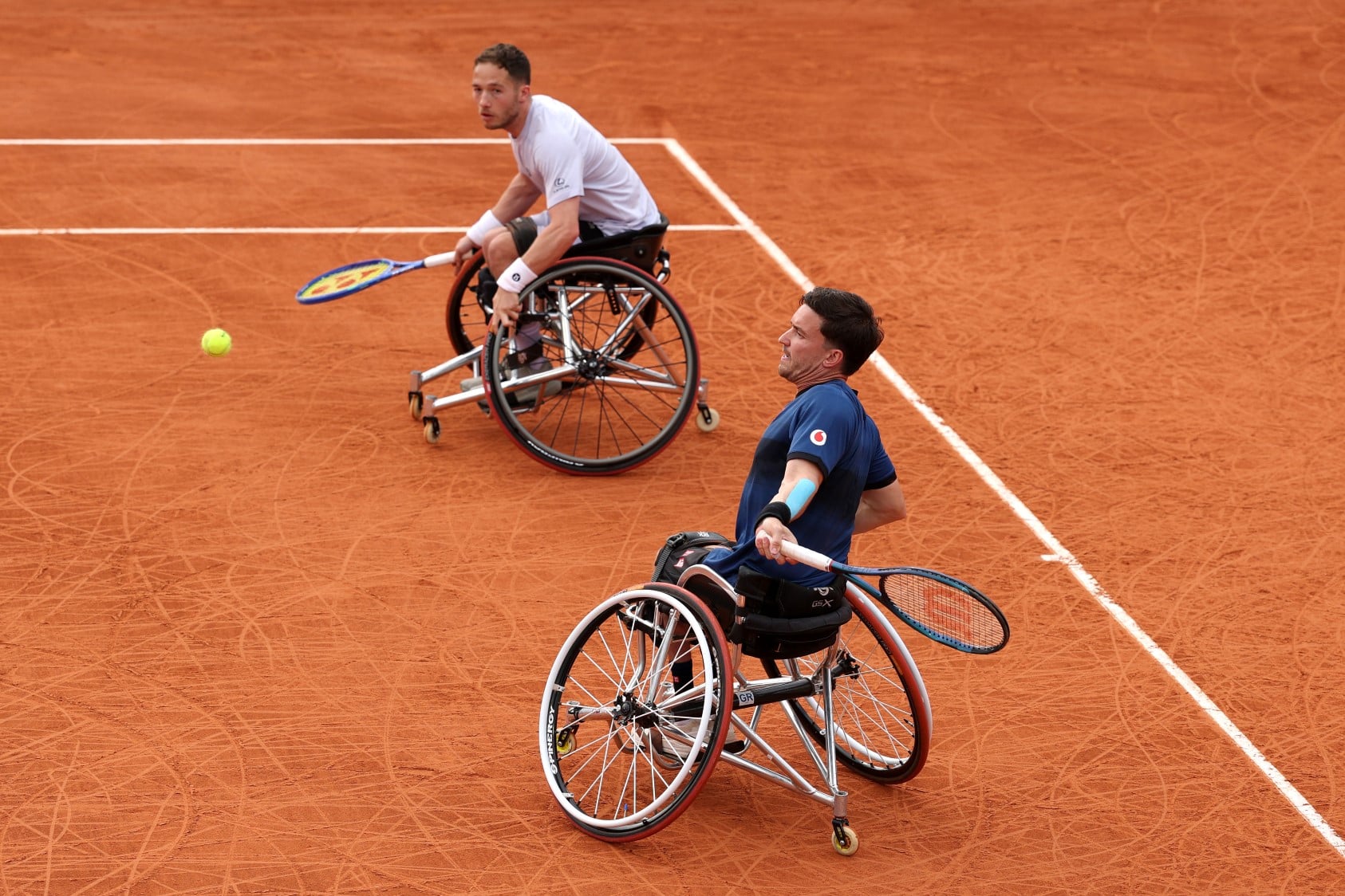 Gordon Reid about to hit a forehand on the clay with his partner Alfie Hewett looking on