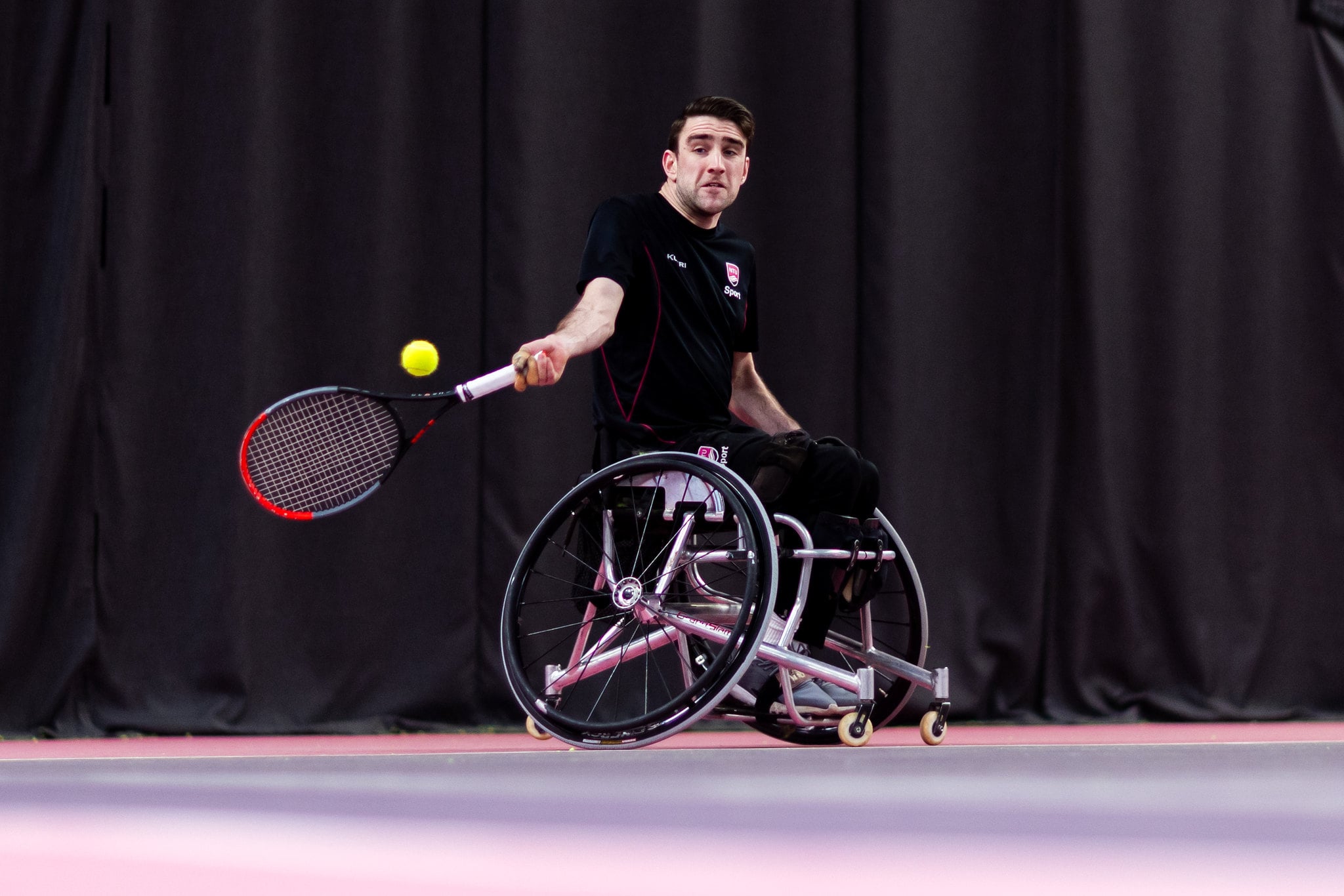 A man in a wheelchair hits a tennis ball