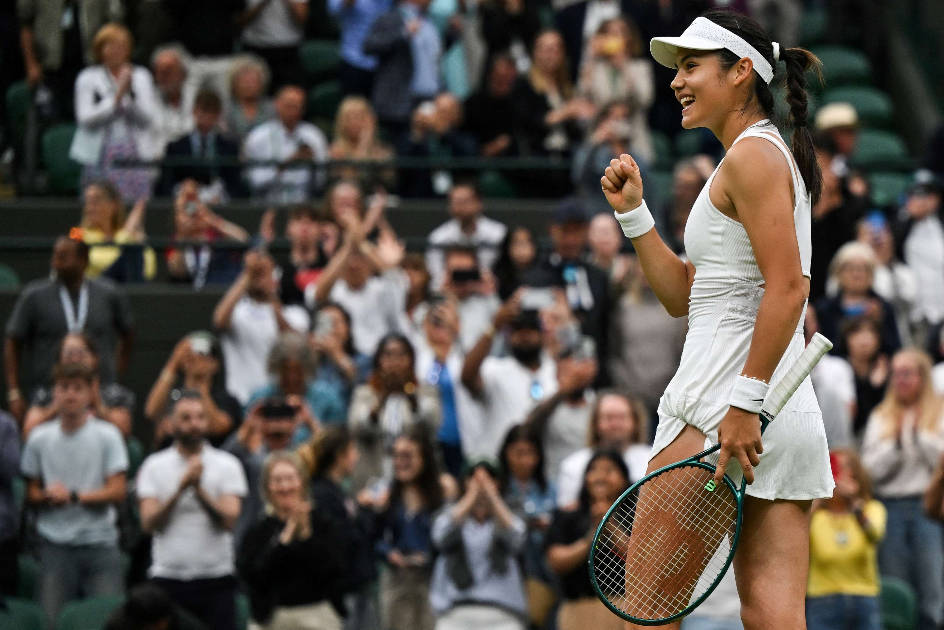 British tennis player Emma Raducanu smiling while tennis fans watch her on Centre Court at Wimbledon