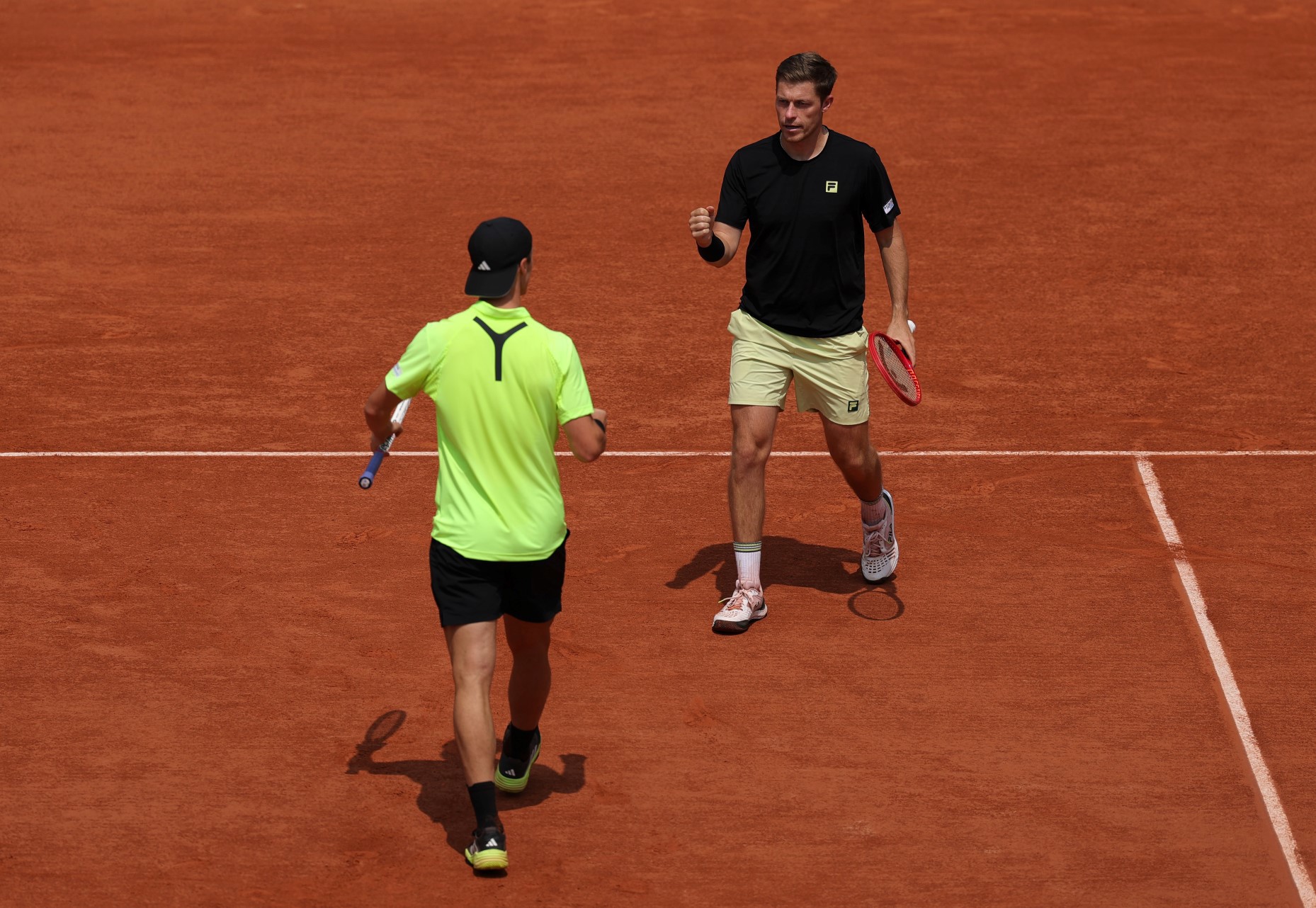 Neal Skupski walking with his fist pumped in celebration towards his partner Joe Salisbury who's doing the same celebration on the Roland Garros clay court