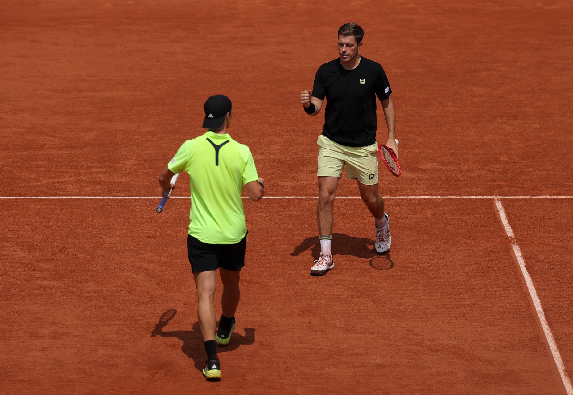 Neal Skupski walking with his fist pumped in celebration towards his partner Joe Salisbury who's doing the same celebration on the Roland Garros clay court