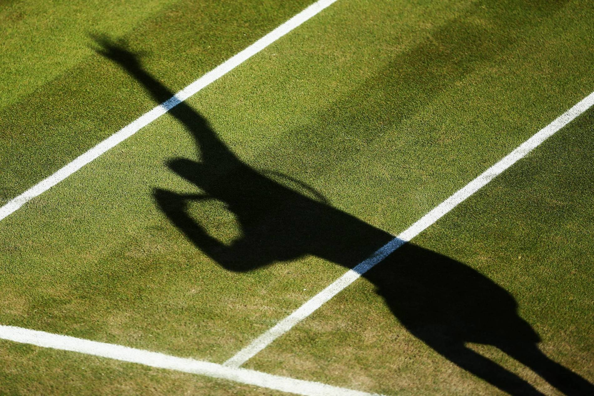Shadow of a tennis player serving on the grass