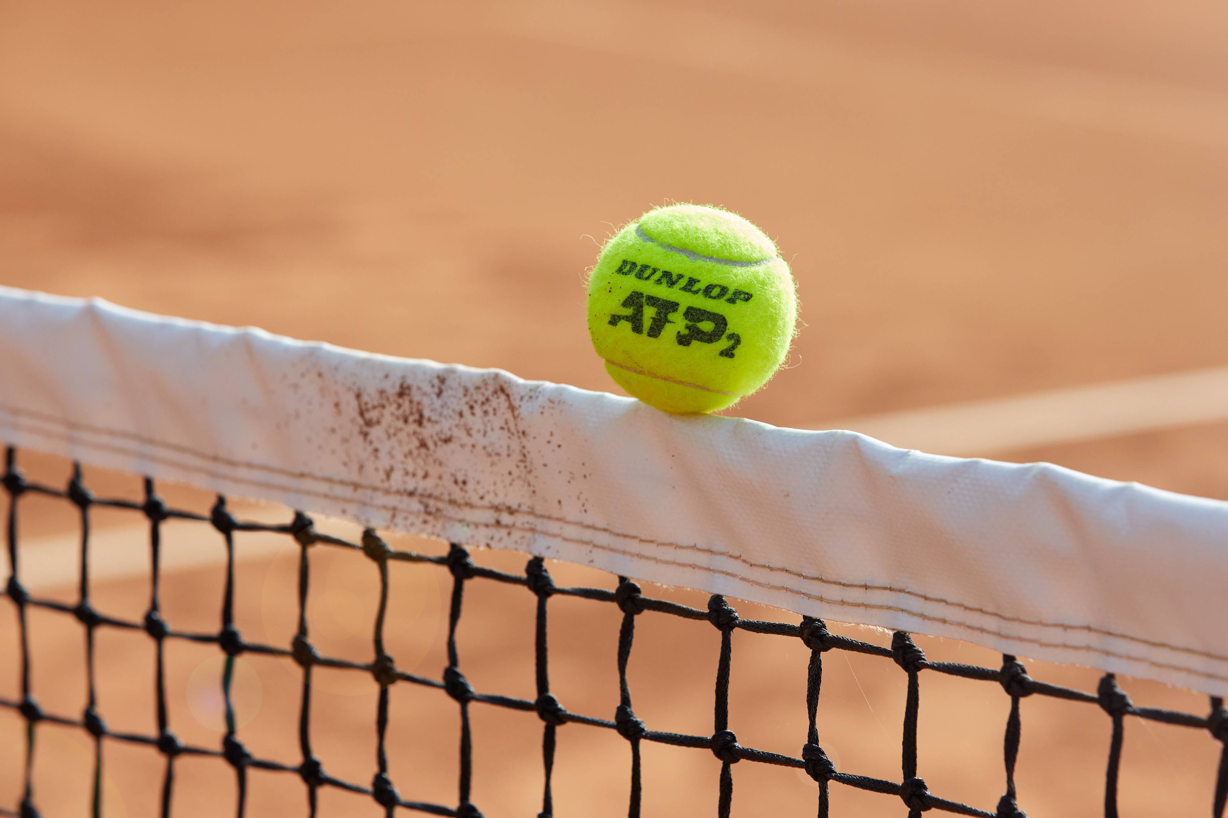 A Dunlop tennis ball balancing on a net cord