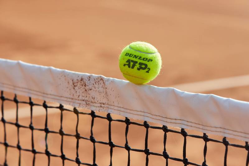 A Dunlop tennis ball balancing on a net cord