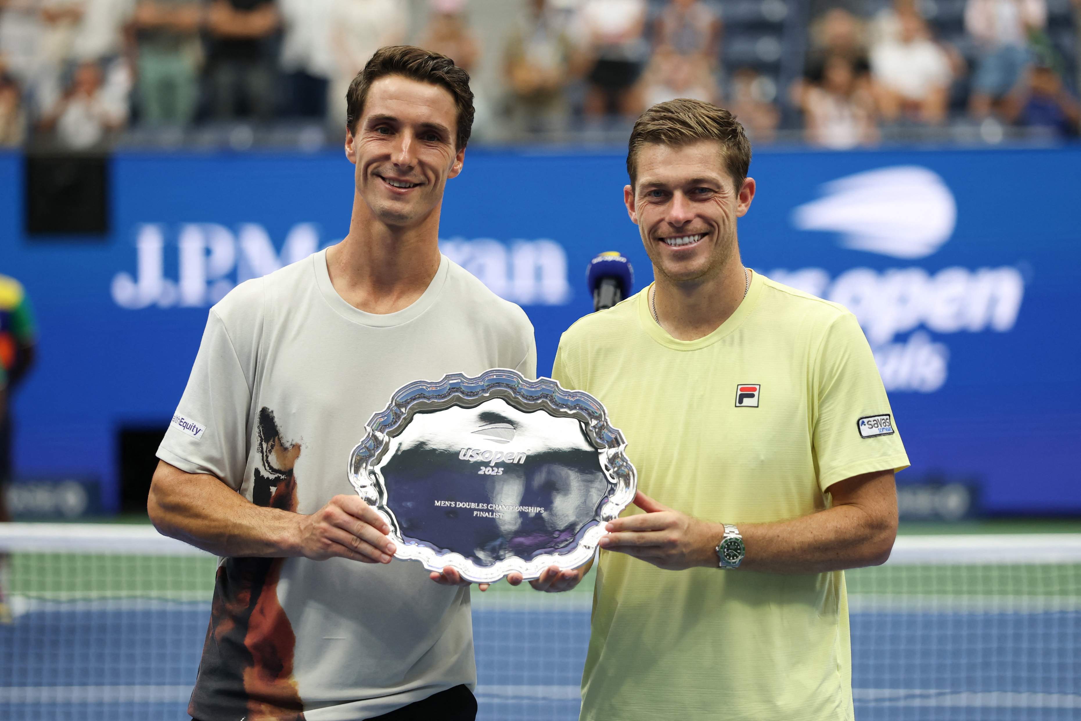 British tennis players Joe Salisbury and Neal Skupski holding their US Open men's doubles runner-up trophy on court