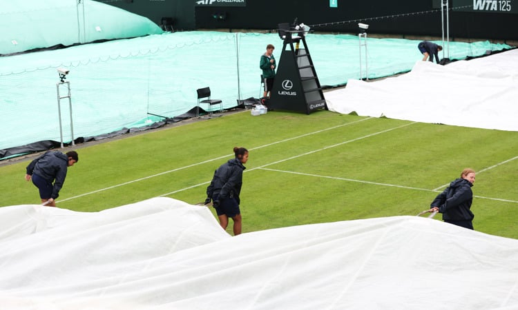 Three grounds staff pull the covers over the court during the rain