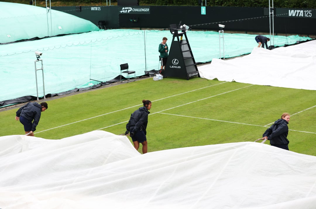 Three grounds staff pull the covers over the court during the rain