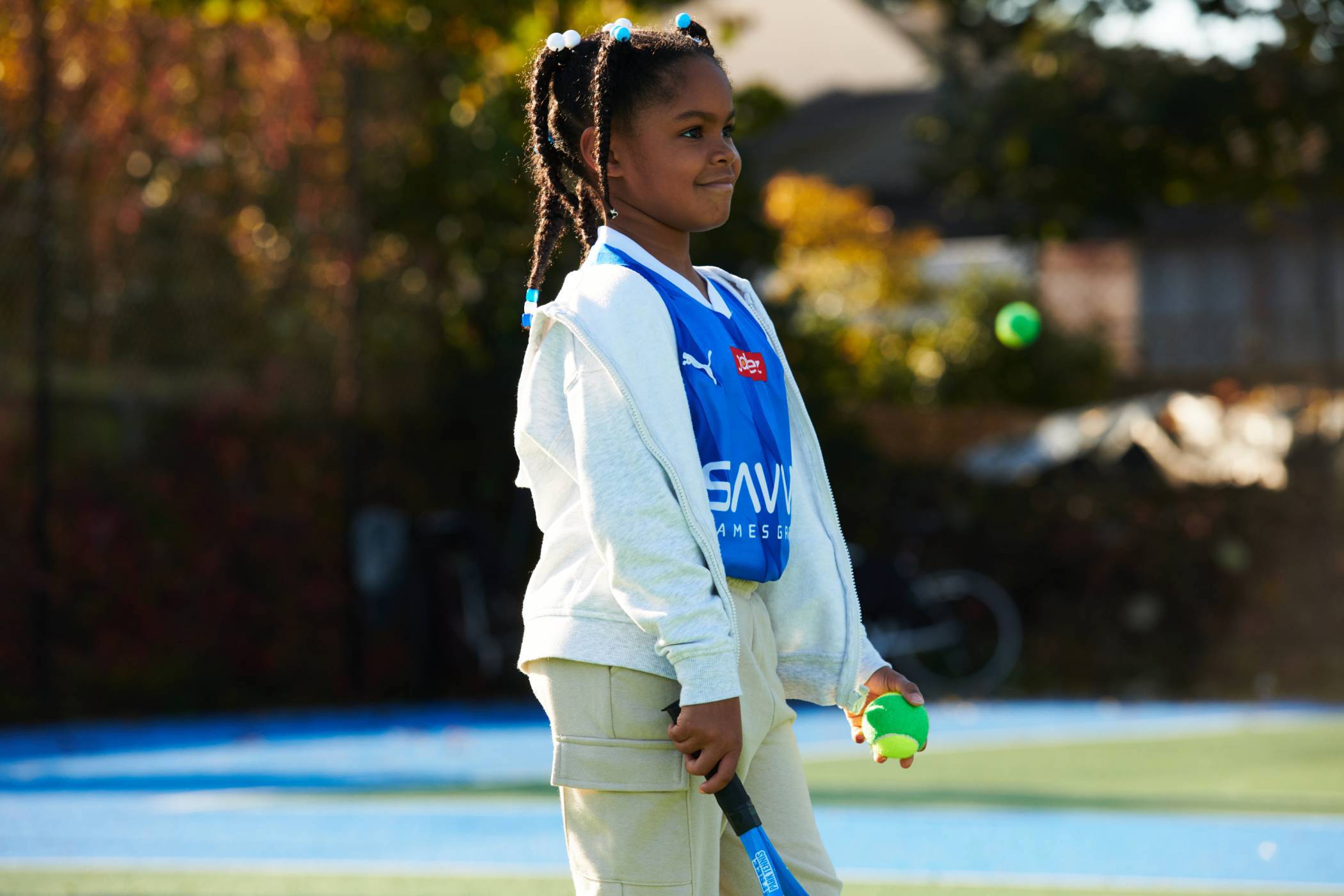 Young girl smiling on court with a tennis racket and ball