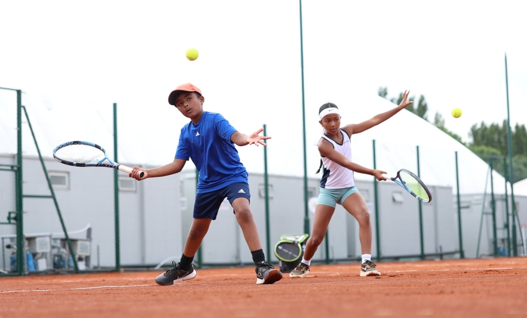 One boy and one girl hitting balls on a clay tennis court