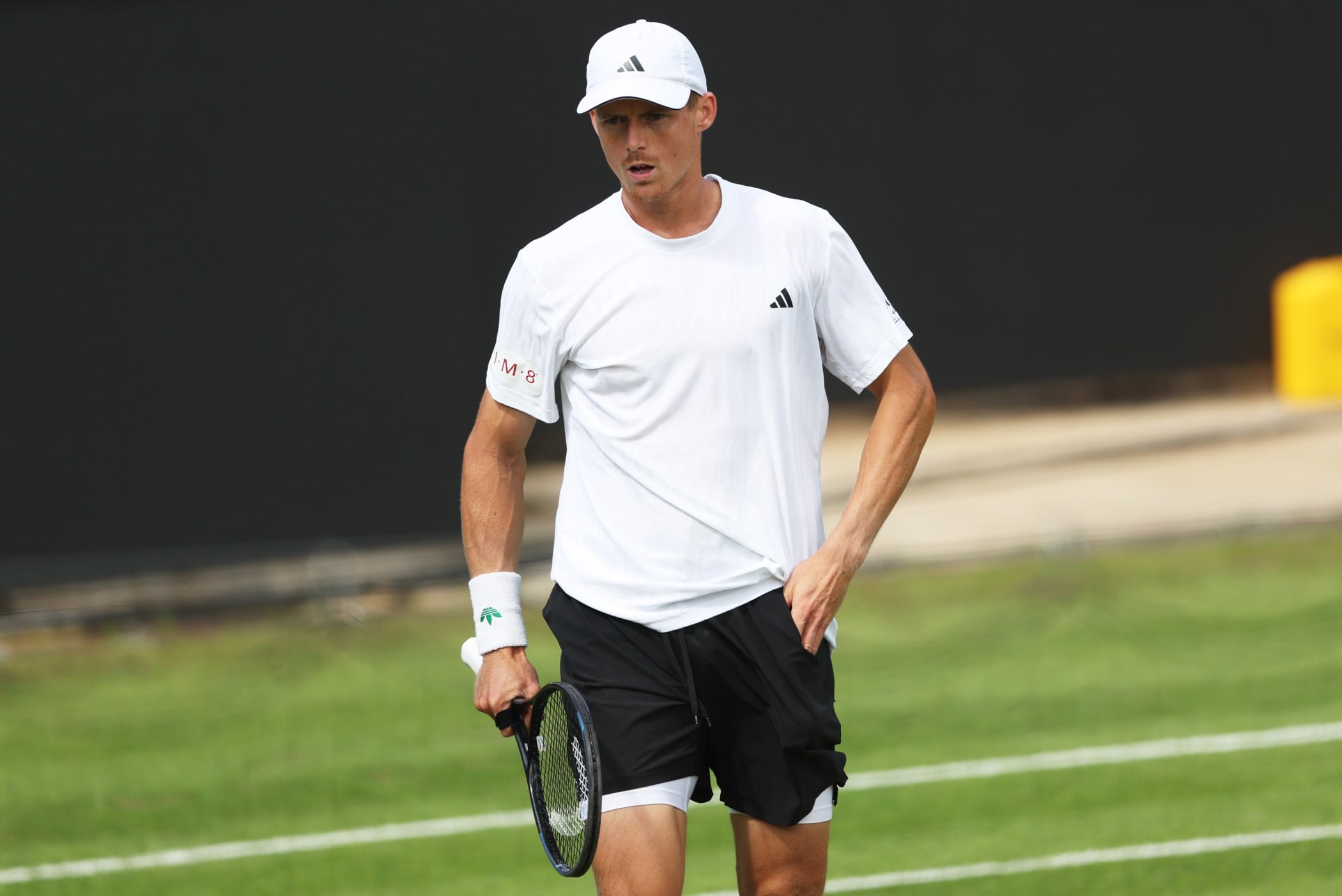 British tennis star Billy Harris holding his tennis racket in one hand and putting his other hand in the pocket of his shorts while stood on a grass tennis court