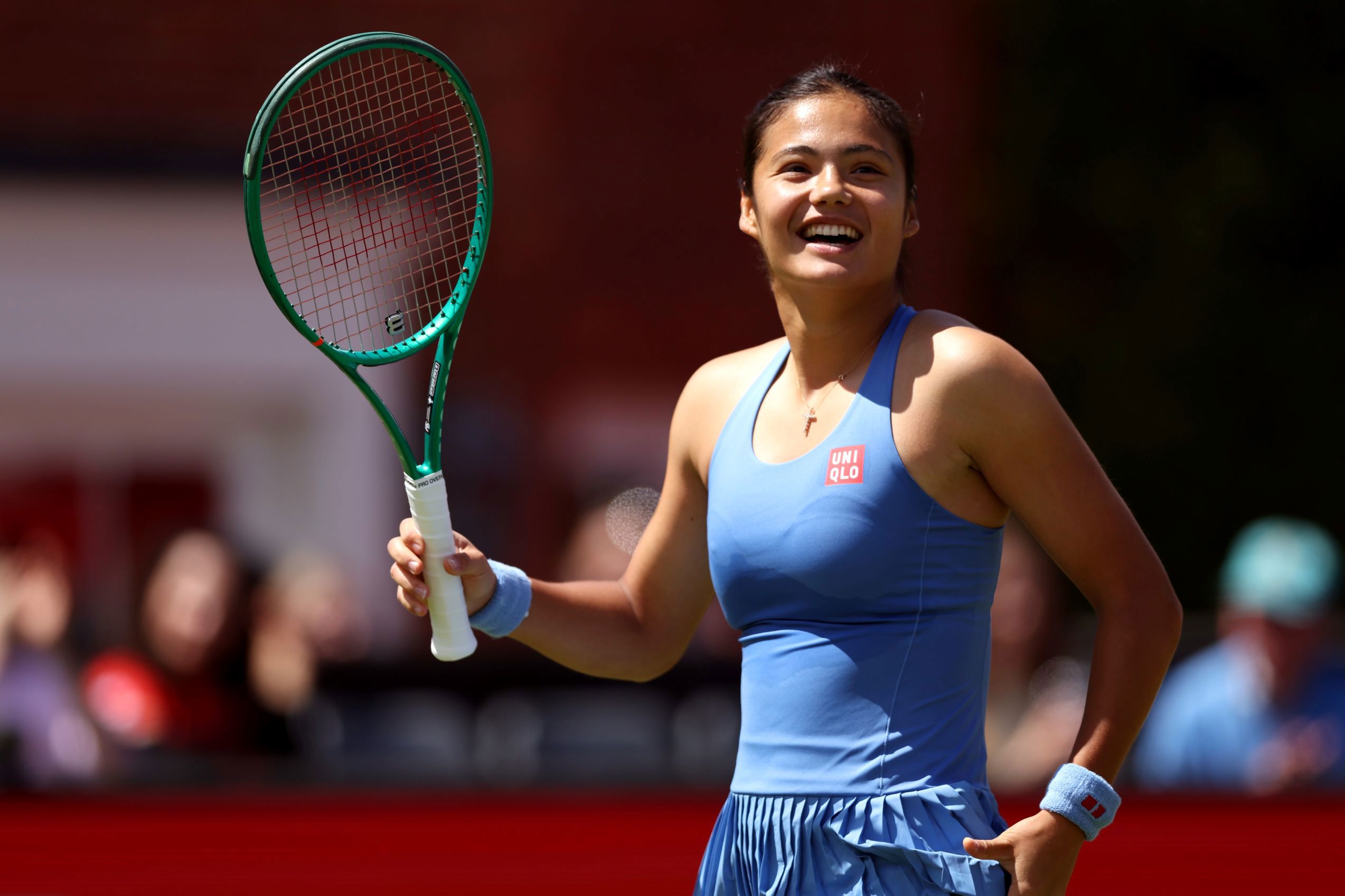 Emma Raducanu smiles and waves her racket in the air on court at the HSBC Championships