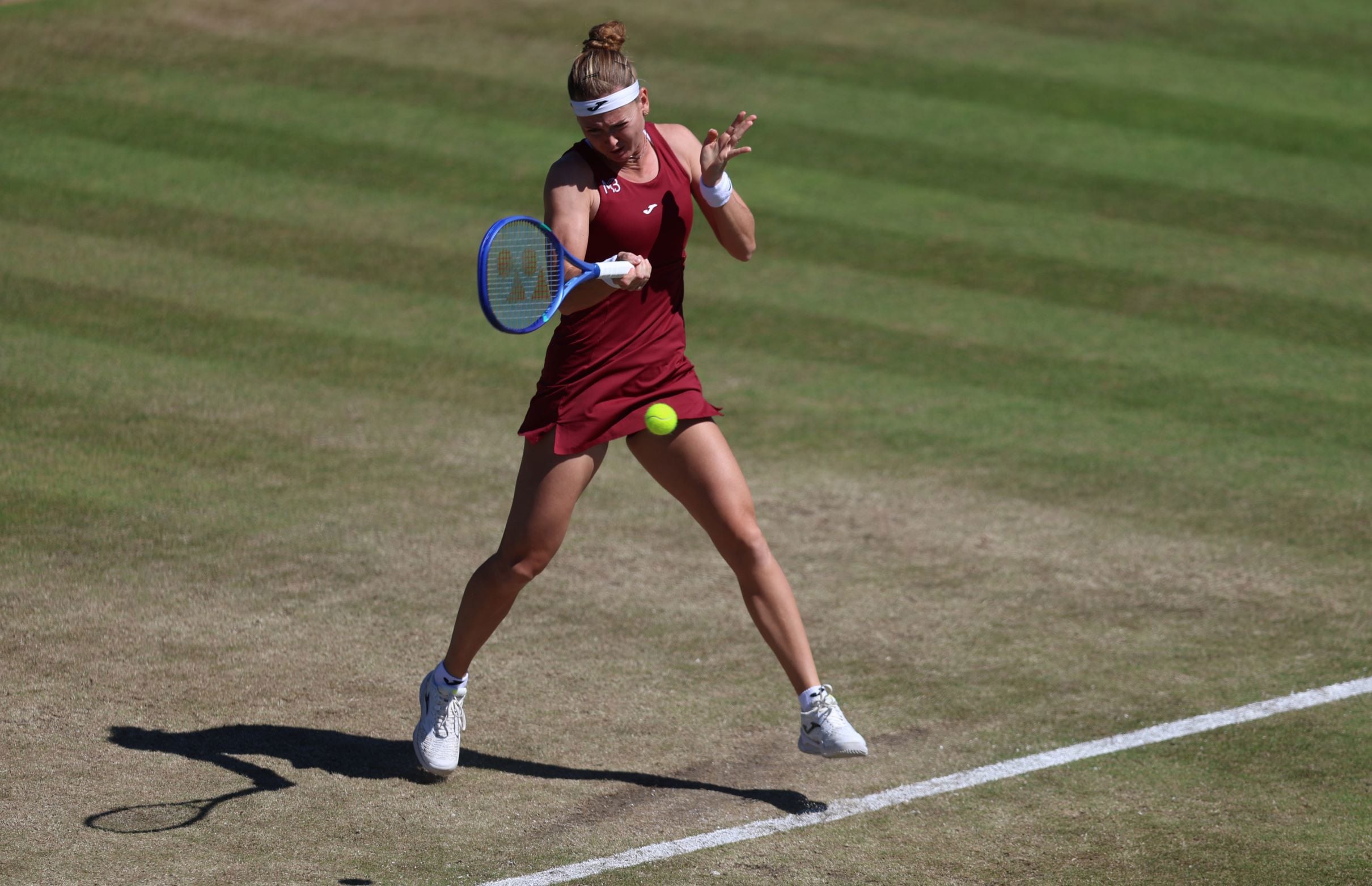 Maria Bouzkova hitting a forehand at the baseline on a grass tennis court