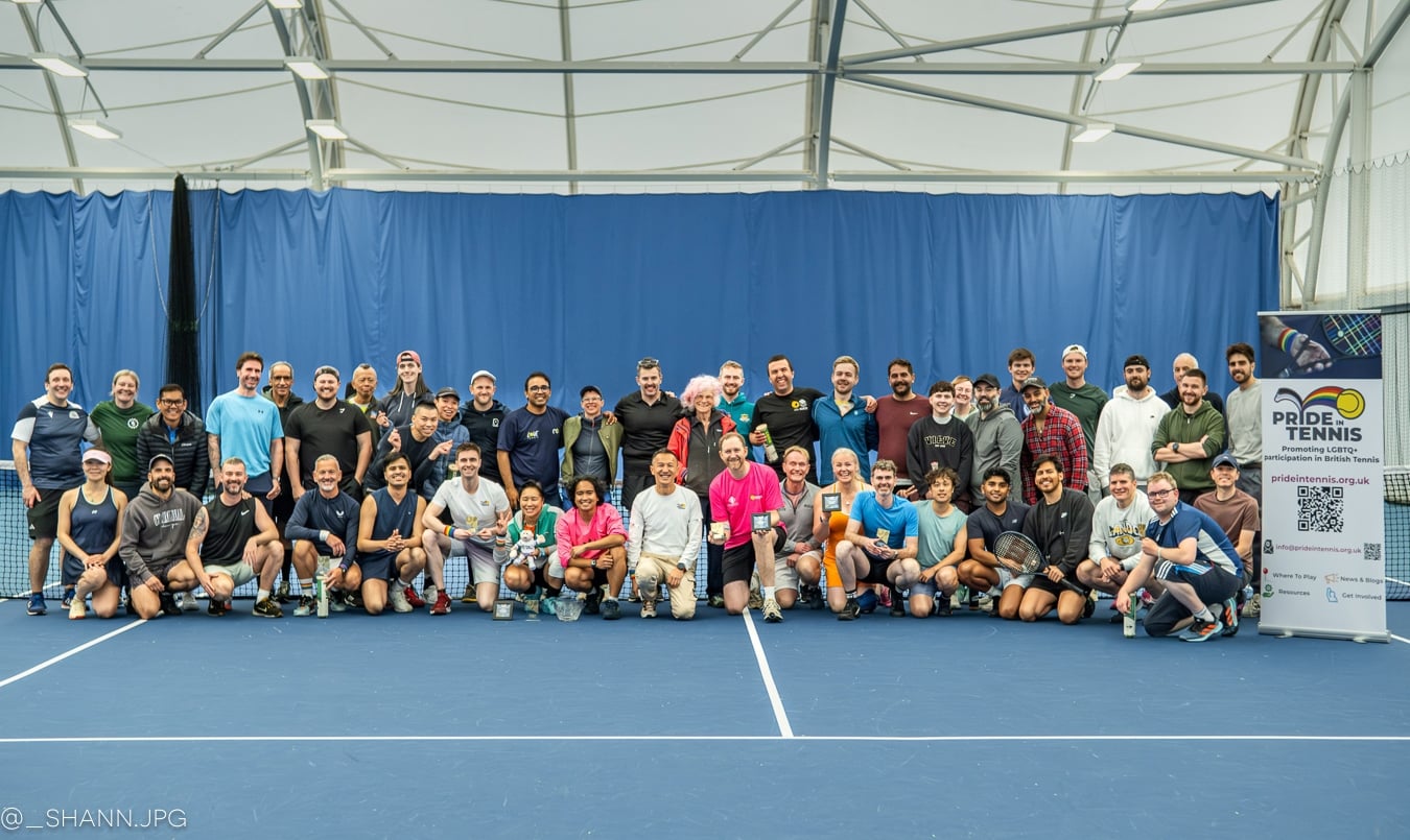 A large group of people pose for a photo on a blue indoor tennis court