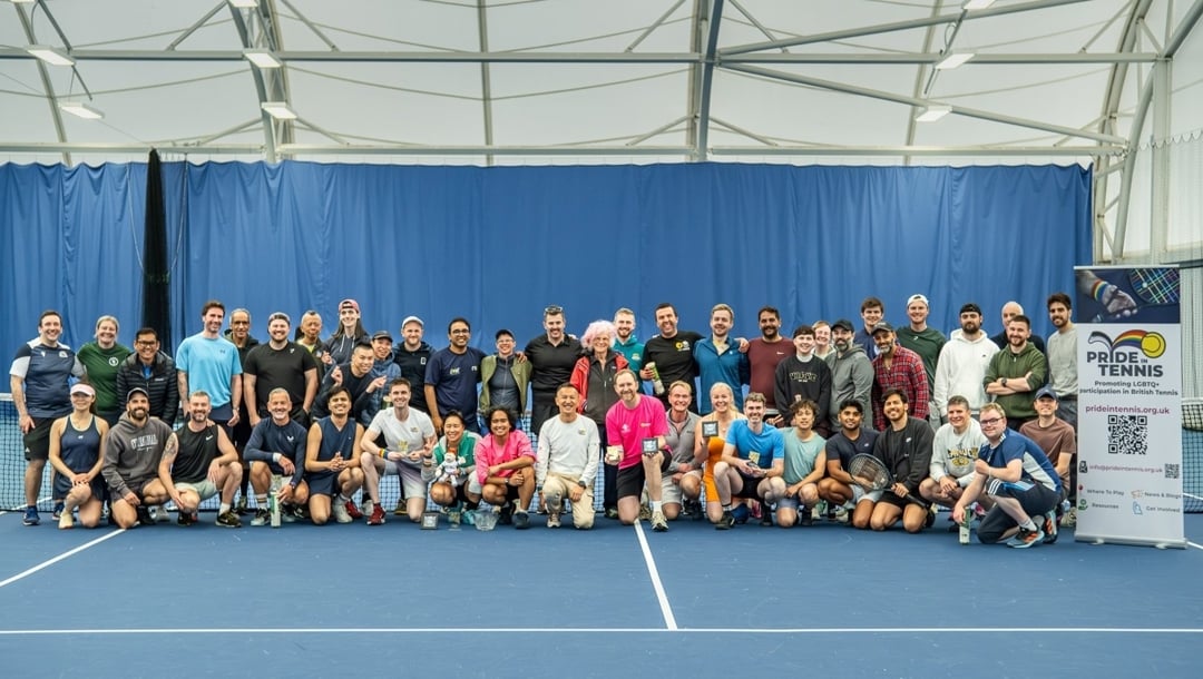 A large group of people pose for a photo on a blue indoor tennis court