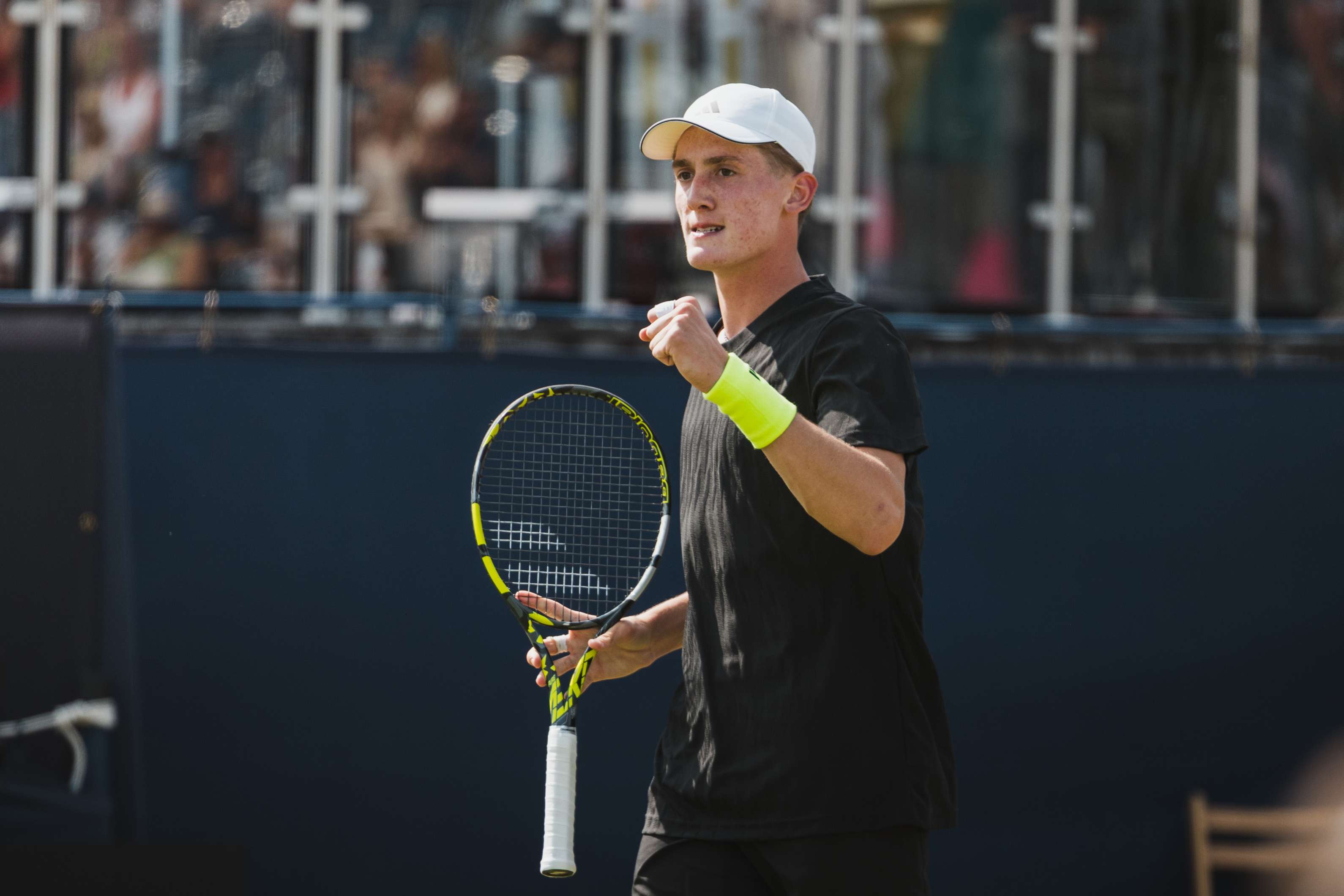 Henry Searle clenching his fist in celebration while holding his tennis racket in the other hand during a match
