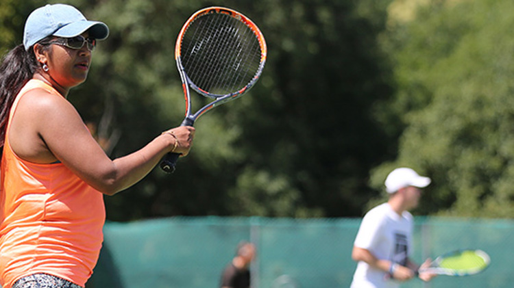 Woman in an orange vest playing tennis on a sunny day