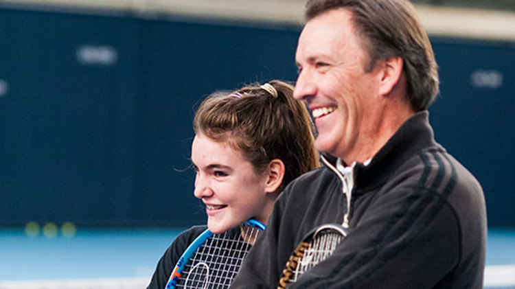 child and adult standing next to each other holding their rackets and smiling 