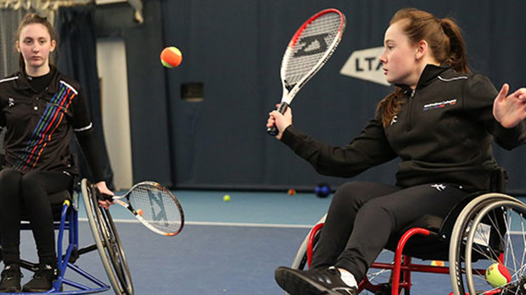 Two women playing wheelchair tennis