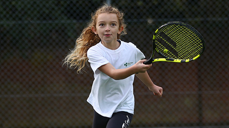 Young girl playing tennis with a black and yellow racket