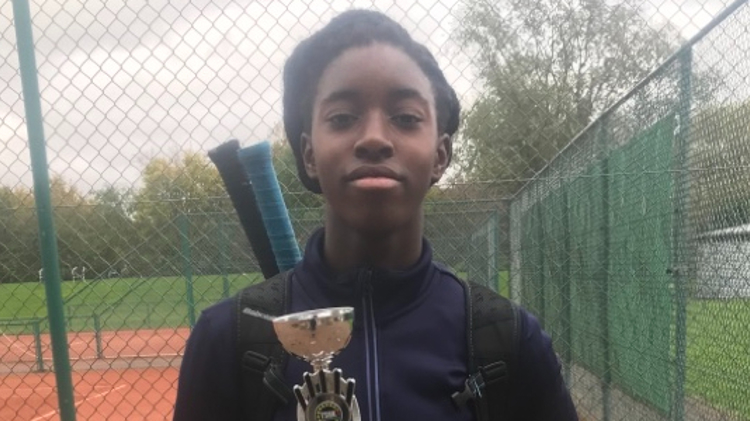 Annis Frimpong holding an award in front of a tennis court