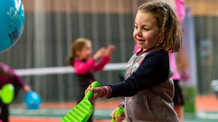 little child playing with plastic green tennis racket hitting blue balloon